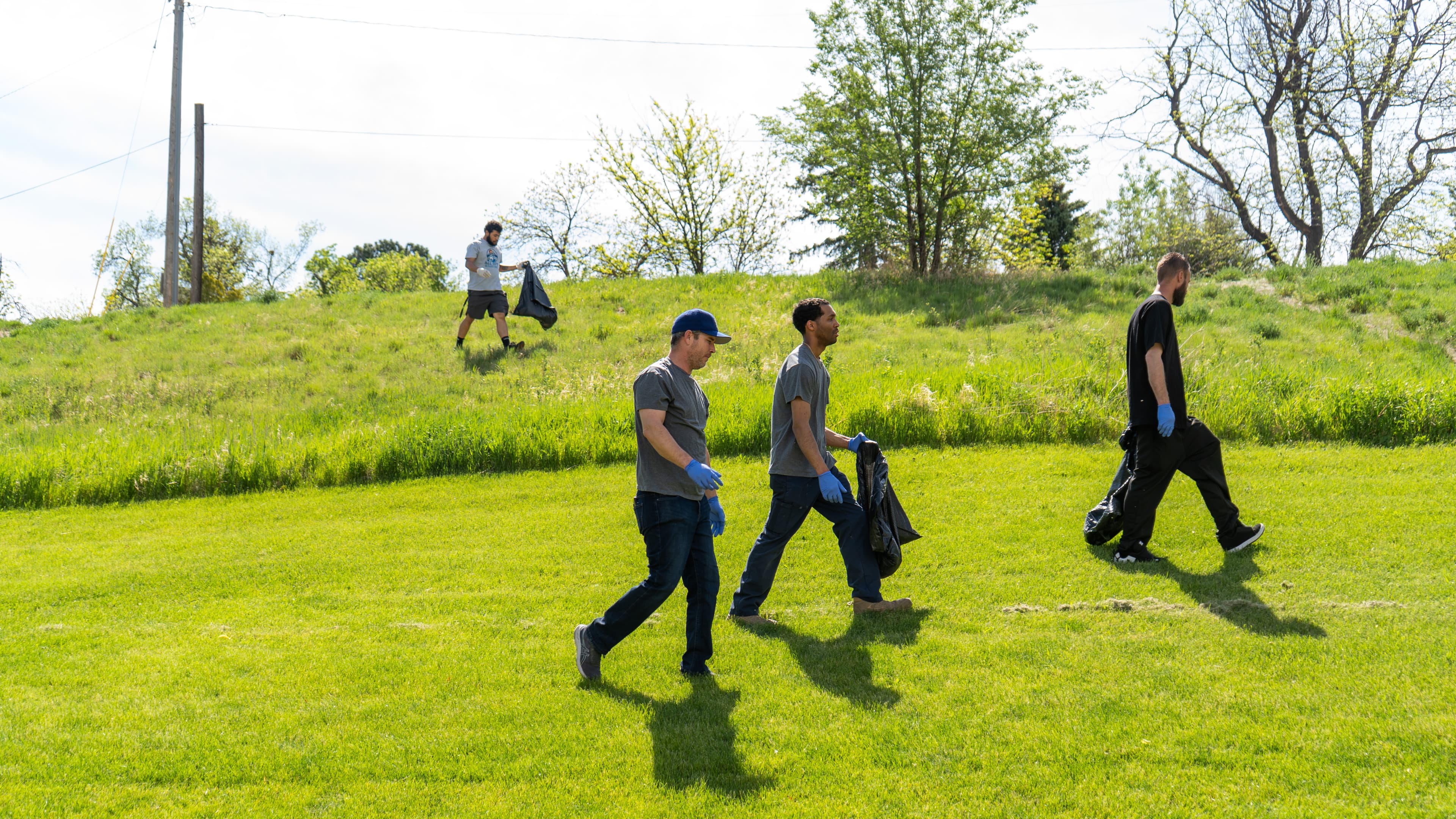 All Out Hauling team members carrying cleanup bags across a green field
